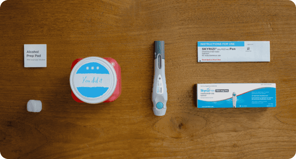 SKYRIZI injection preparation: alcohol pad, cotton ball, Sharps Mail-back Disposal Kit, skyrizi pen, box, and box insert arranged on a table.